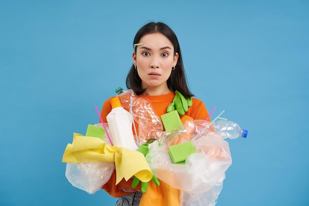 Photo gratuite une fille asiatique confuse ne sait pas comment recycler une femme détient des ordures en plastique avec un visage choqué bleu ba