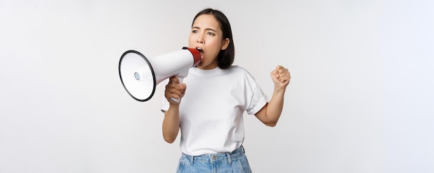 Fille asiatique criant au mégaphone jeune activiste protestant à l'aide d'un haut-parleur fort debout sur fond blanc Copier l'espace