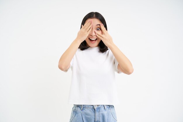 Une fille asiatique excitée regarde avec un visage surpris qui regarde à travers les doigts attend que la surprise se dresse sur wh