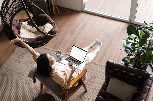 Une fille asiatique heureuse et insouciante a fini de travailler et a l'air satisfaite assise à la maison avec un ordinateur portable ...