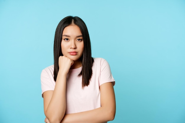 Fille asiatique regardant smth ennuyeux regardant avec une expression de visage réticente non amusée debout en t-shirt o...