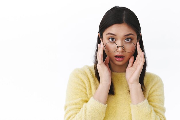 Une fille asiatique surprise laisse tomber la mâchoire et les lunettes de décollage étonnée d'entendre des nouvelles étonnantes choquantes entendre une histoire incroyable bavarder avec les membres de l'équipe au travail debout impressionné fond blanc