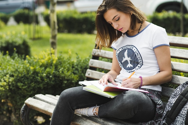 Photo gratuite fille assise sur banc d'écriture dans un cahier
