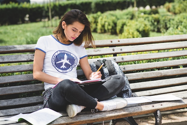 Fille assise sur banc en parc en train d&#39;étudier