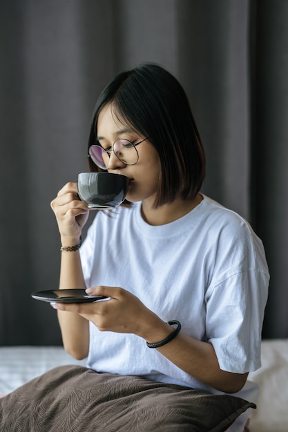 Une fille assise et buvant du café dans la chambre.