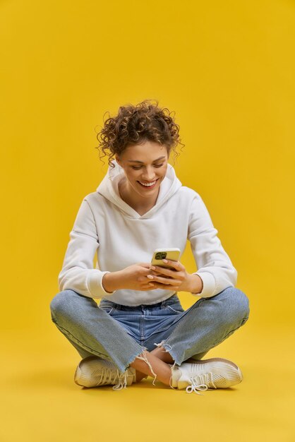 Fille assise dans la pose de lotos à l'aide d'un smatphone