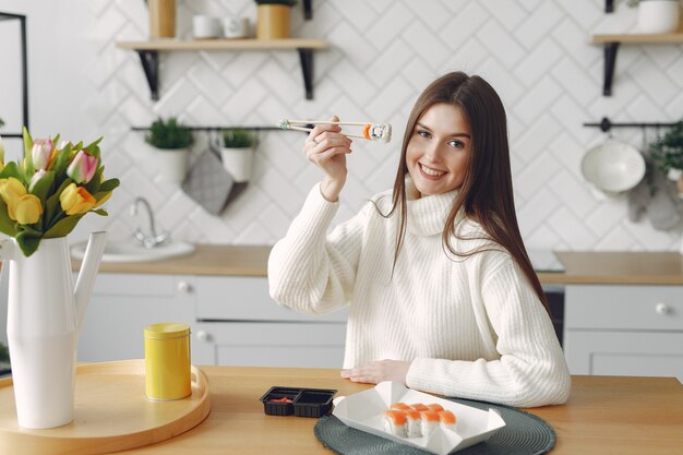 Fille assise à la maison à la table avec un sushi