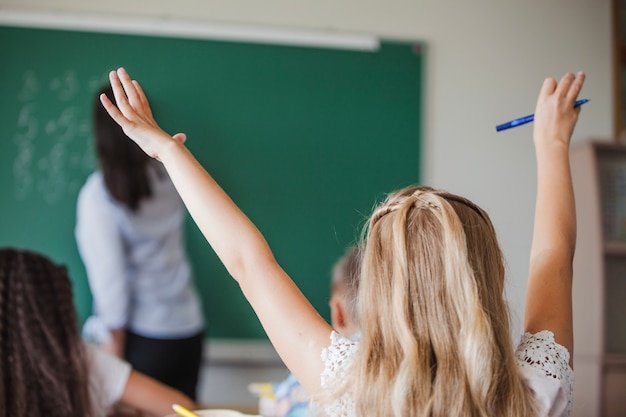 Fille assise en salle de classe en levant la main