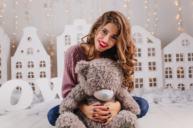 Fille assise sur le sol avec des sourires et des câlins mignons maquillage lumineux ours en peluche gris