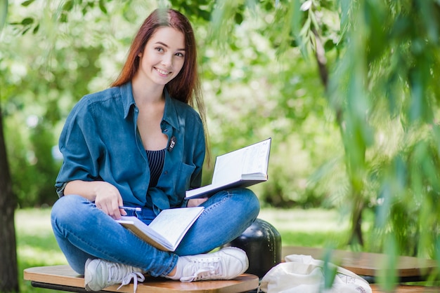 Fille assise sur table avec un livre de texte souriant