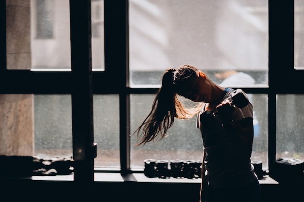 Fille athlétique mince effectue des exercices physiques avec des haltères.