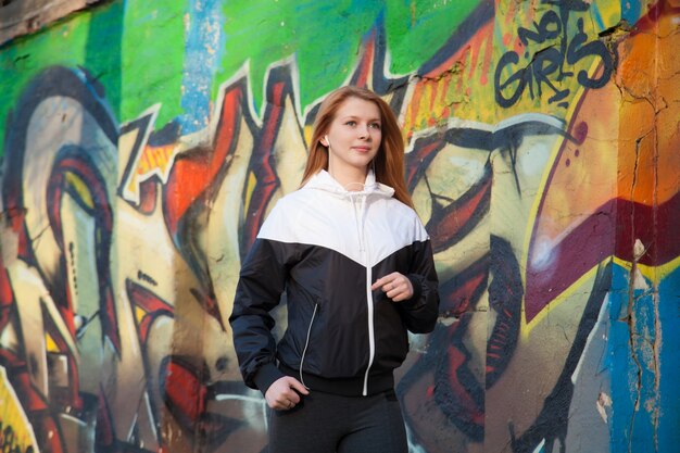 Une fille athlétique qui marche par un mur de graffiti brillant