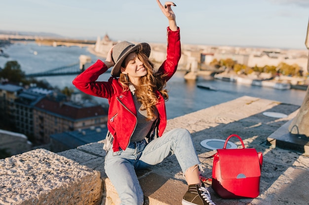 Fille au chapeau élégant et pantalon vintage drôle posant sur fond de rivière