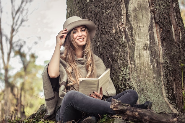 fille au chapeau lisant un livre dans la forêt d'automne