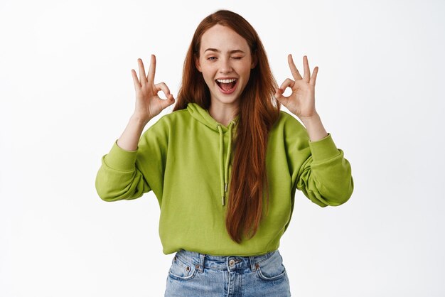 Une fille au gingembre souriante qui rit en montrant des signes d'accord et a l'air heureuse d'approuver et de ne dire aucun problème comme et de louer quelque chose sur fond blanc