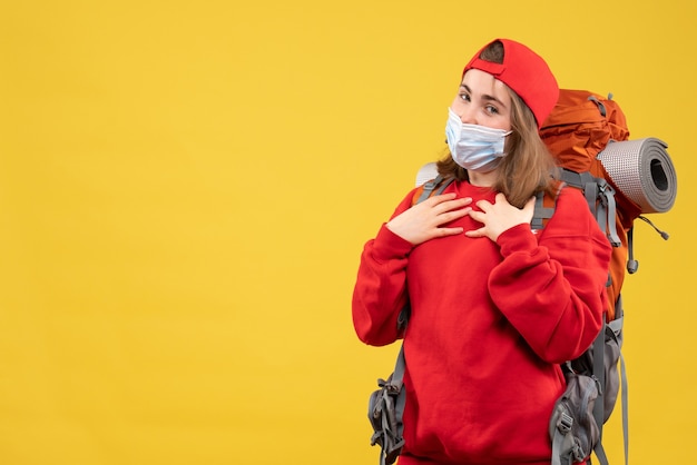 Fille d'auto-stoppeur vue de face avec sac à dos et masque mettant les mains sur sa poitrine