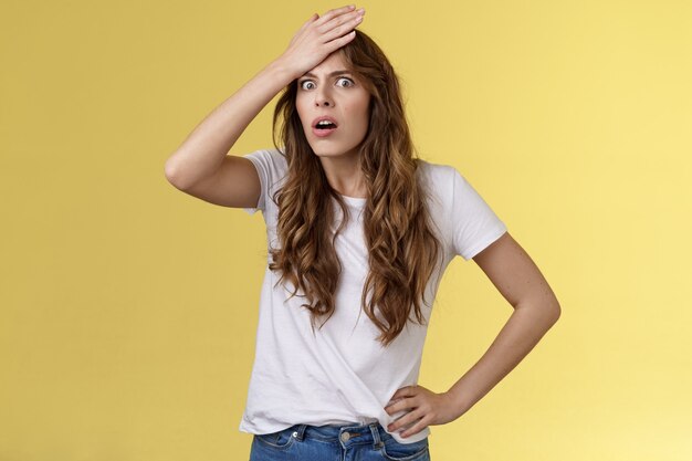 Fille aux cheveux bouclés choquée en détresse angoissée réalisant faire une erreur stupide coup de poing front haletant grimace grimace dérangée toucher le visage bouleversé se souvenir d'une tâche importante