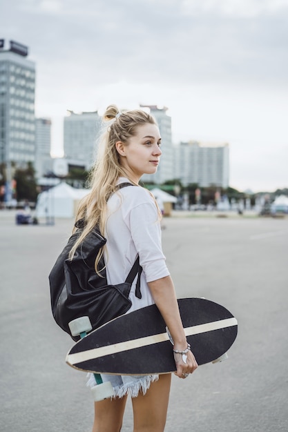 Photo gratuite fille aux cheveux longs patins sur une planche à roulettes. rue, sports actifs