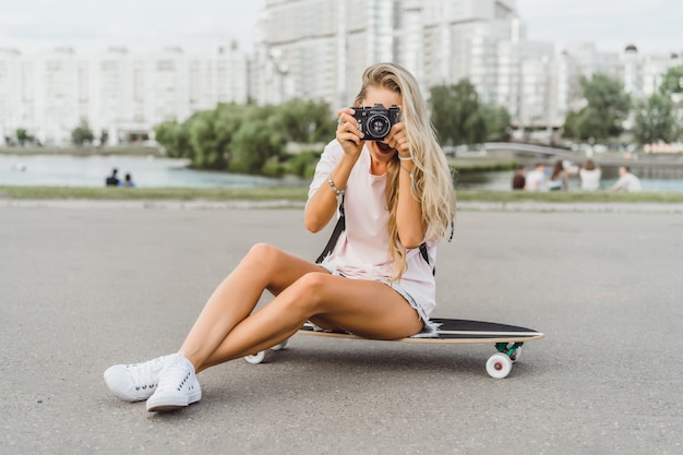 fille aux cheveux longs avec skateboard photographiant à la caméra. rue, sports actifs