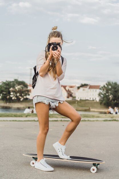 fille aux cheveux longs avec skateboard photographiant à la caméra. rue, sports actifs