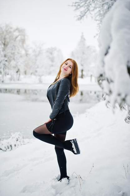 Fille aux cheveux rouges en manteau de fourrure marchant au parc enneigé d'hiver