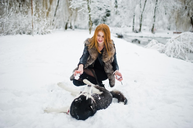 Fille aux cheveux rouges marchant au parc avec un chien husky le jour de l'hiver