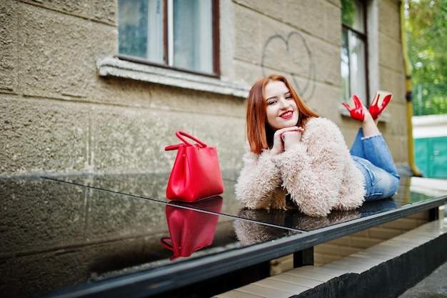 Fille aux cheveux rouges avec sac à main rouge posé à la rue de la ville