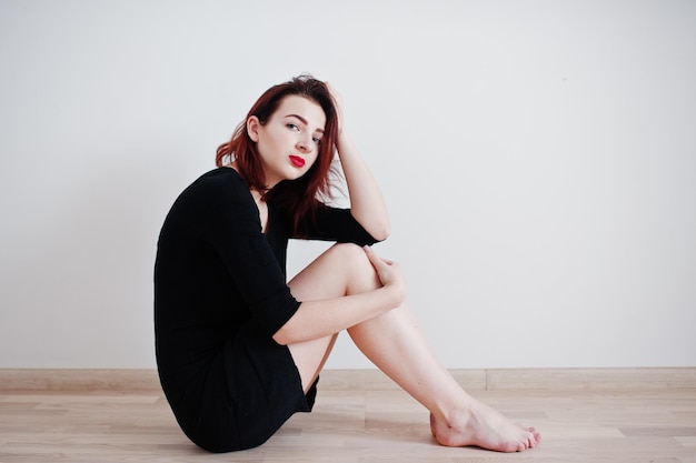 Fille aux cheveux rouges sur une tunique de robe noire contre un mur blanc dans une salle vide