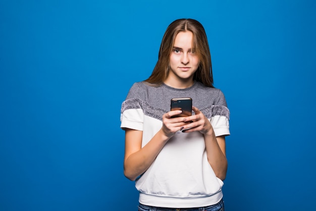 Fille aux grands yeux à l'aide de nouveau téléphone devant le mur bleu