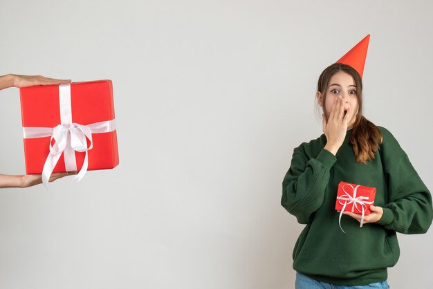 Fille aux yeux écarquillés avec partie pointant sur son cadeau de Noël mains humaines tenant cadeau sur blanc