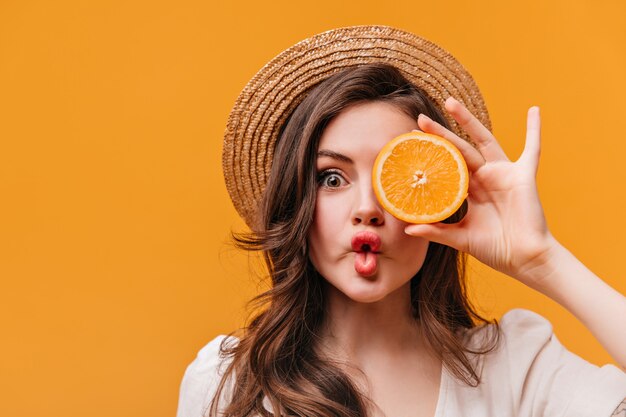 Fille aux yeux verts en canotier fait la grimace et couvre les yeux à moitié orange.