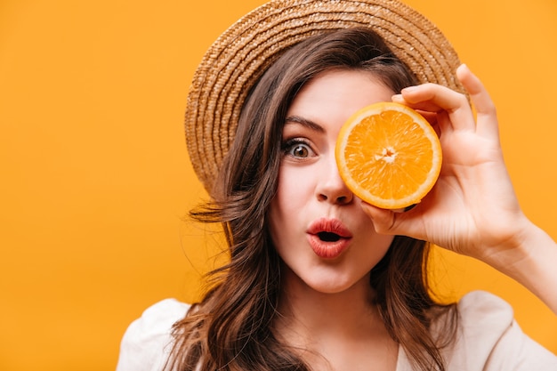 Fille aux yeux verts avec des cheveux ondulés regarde la caméra avec surprise et se couvre les yeux d'orange.