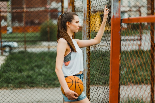 Fille avec un ballon de basket à côté de la clôture