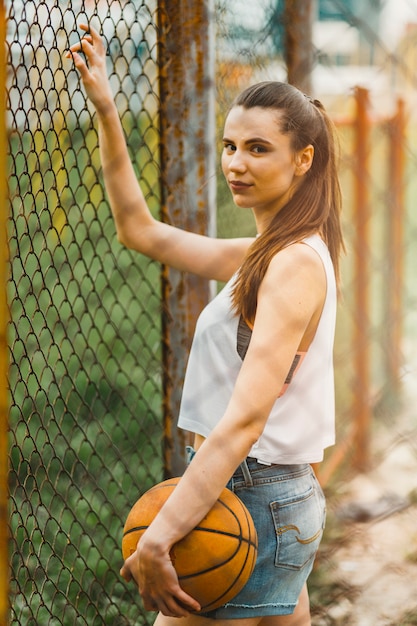 Photo gratuite fille avec un ballon de basket à côté de la clôture