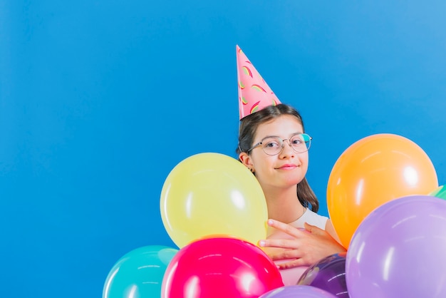 Fille avec des ballons colorés en regardant la caméra sur fond bleu