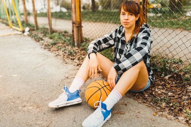 Fille avec basket assis devant la clôture