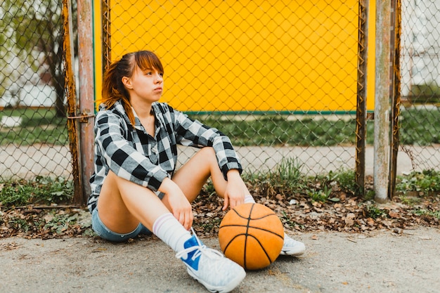 Photo gratuite fille avec basket assis devant la clôture