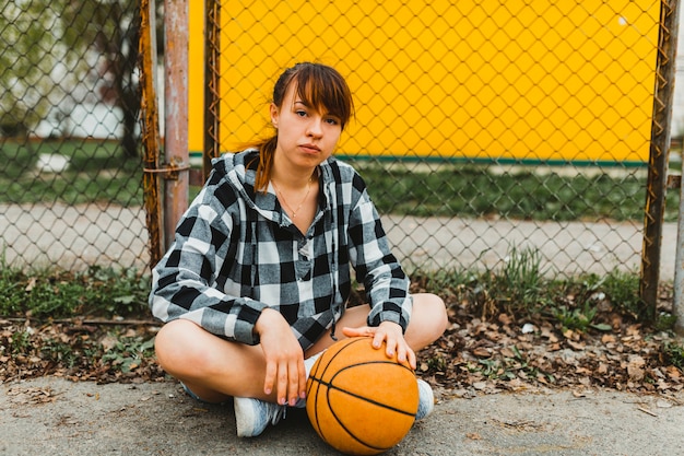 Photo gratuite fille avec basket assis devant la clôture