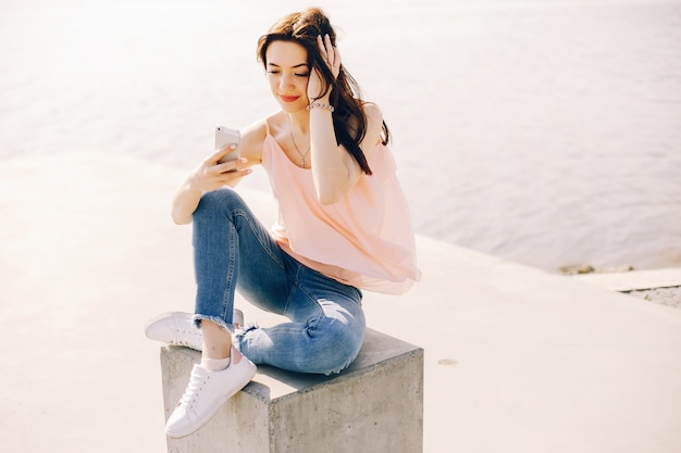 fille belle et lumineuse en t-shirt rose et jeans bleus, assis dans le parc d&#39;été ensoleillé