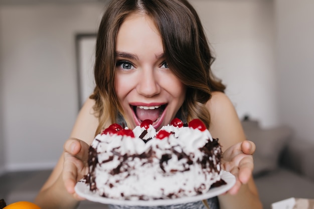 Fille blanche drôle posant avec un délicieux gâteau d'anniversaire. Plan intérieur d'un modèle féminin excité tenant une tarte au chocolat avec des baies.