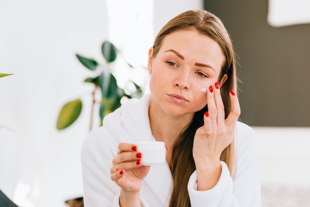 Fille blonde en appliquant la crème sur son visage