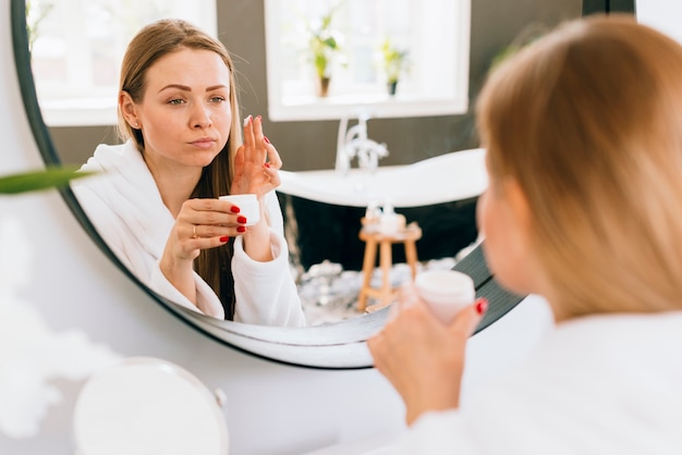 Fille blonde en appliquant la crème sur son visage