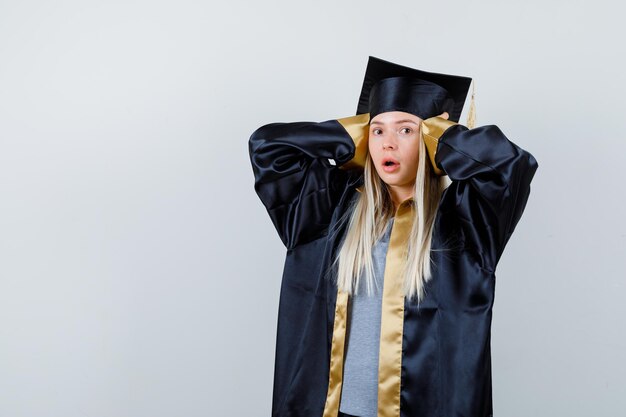 Fille blonde en appuyant sur les mains sur les oreilles en robe de graduation et casquette et à la surprise