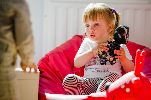 Fille blonde assise dans une chaise avec un dinosaure