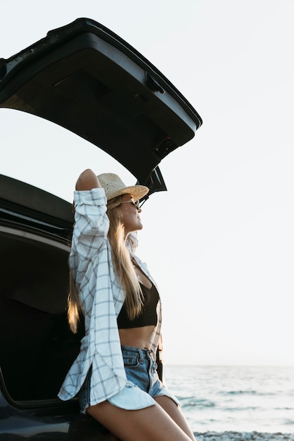 Fille blonde assise dans le coffre d'une voiture près de la mer