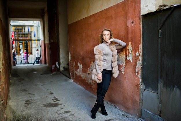 Fille blonde au manteau de fourrure posé contre le vieux mur orange