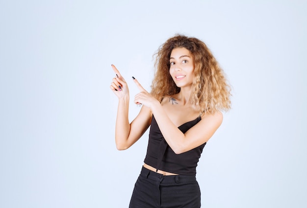 Photo gratuite fille blonde aux cheveux bouclés pointant vers la gauche.