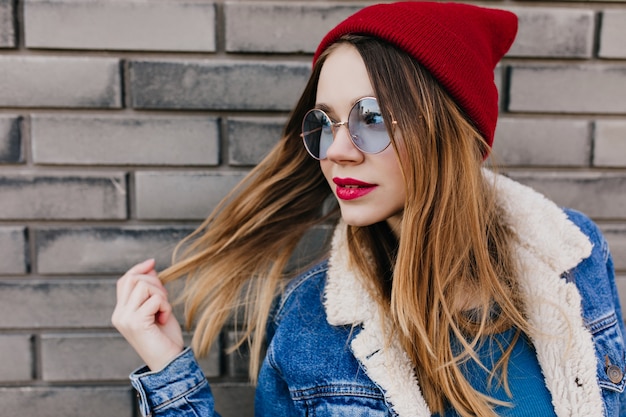 Fille blonde blanche avec un maquillage à la mode posant de manière ludique sur la rue urbaine. Portrait de belle jeune femme en veste en jean, passer du temps à l'extérieur.