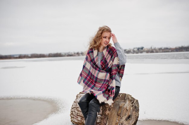 Fille blonde bouclée en plaid à carreaux contre le lac gelé au jour d'hiver