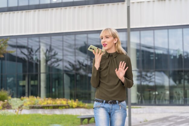 Fille blonde caucasienne d'entrepreneur dans un parc d'affaires faisant un appel avec le téléphone, lieu de travail moderne parmi la nature